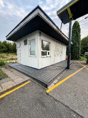 Small white building with a terrace deck on a paved area with yellow lines