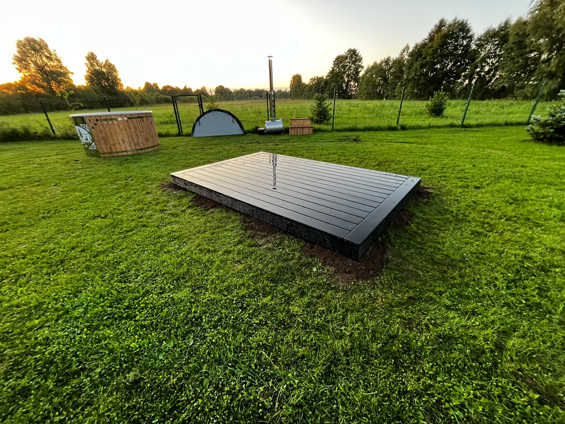 Outdoor hot tub with wooden steps in a grassy field under a blue sky with clouds.