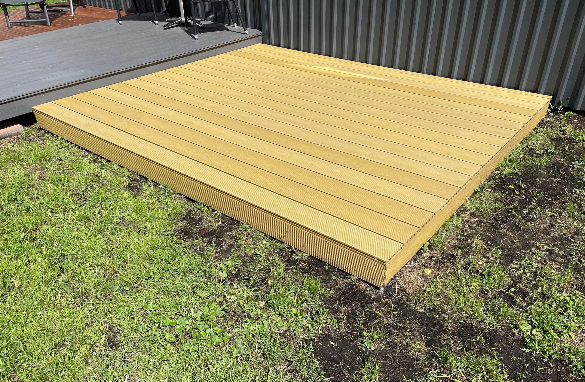 Wooden deck on grass with a corrugated metal wall in the background